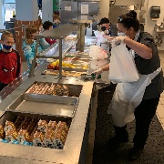 Cafeteria worker preparing bag of food for boy